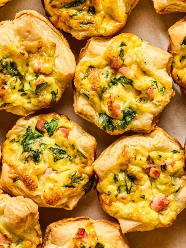Mini quiches with puff pastry on plate topped with onion and chopped parsley.