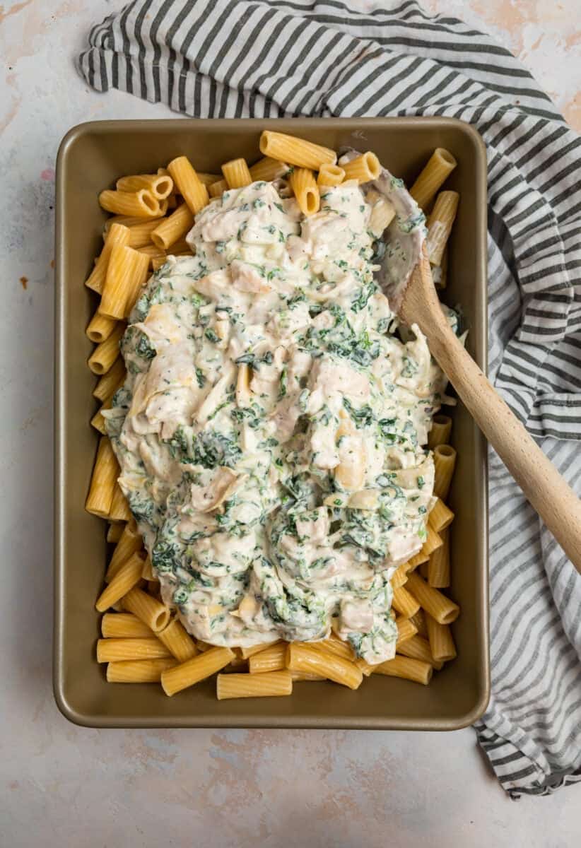 Spinach artichoke and chicken mixture over past in pan.