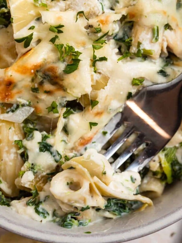 Chicken spinach and artichoke pasta casserole in dish with fork.