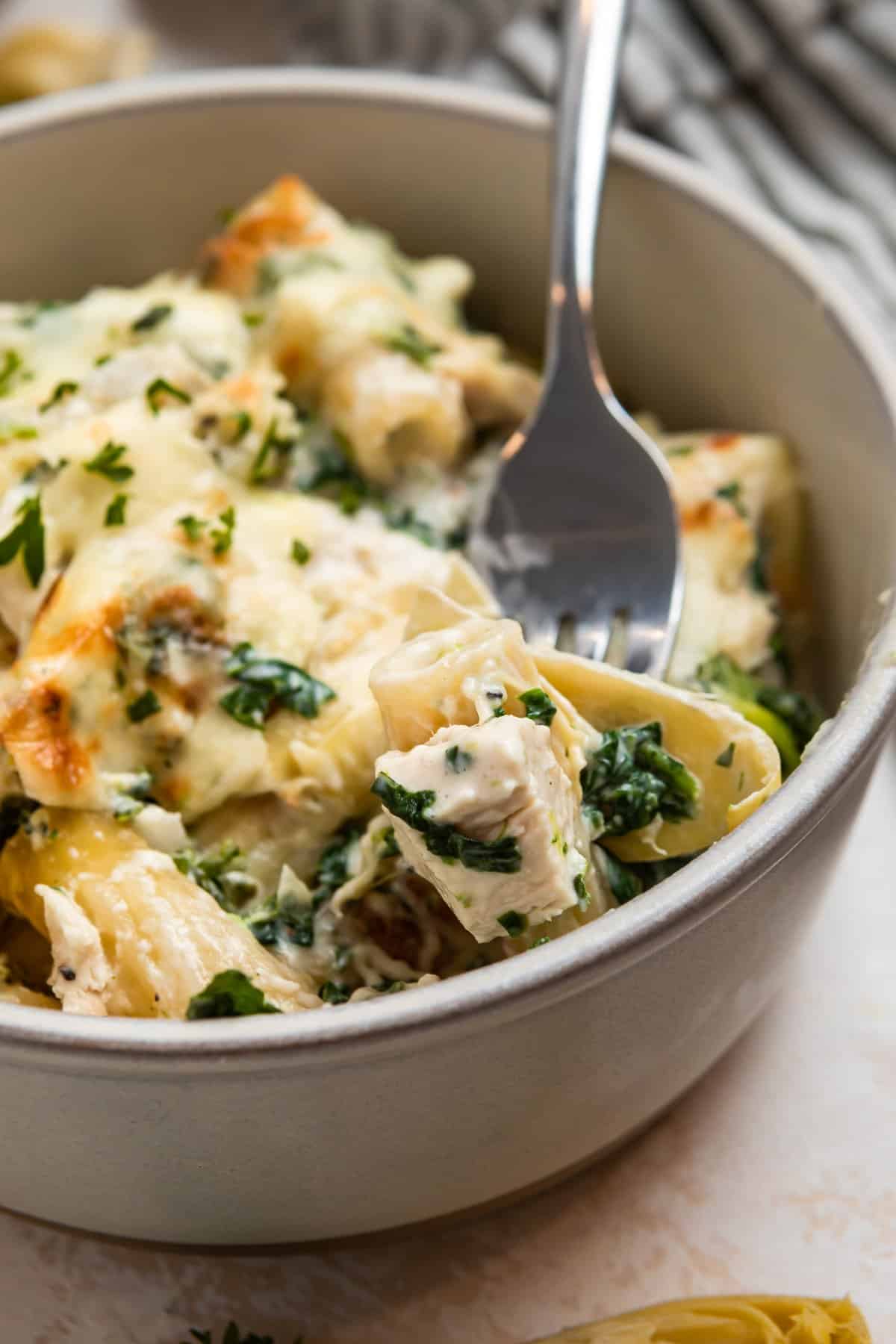 Spinach, chicken artichoke pasta casserole in bowl with fork.