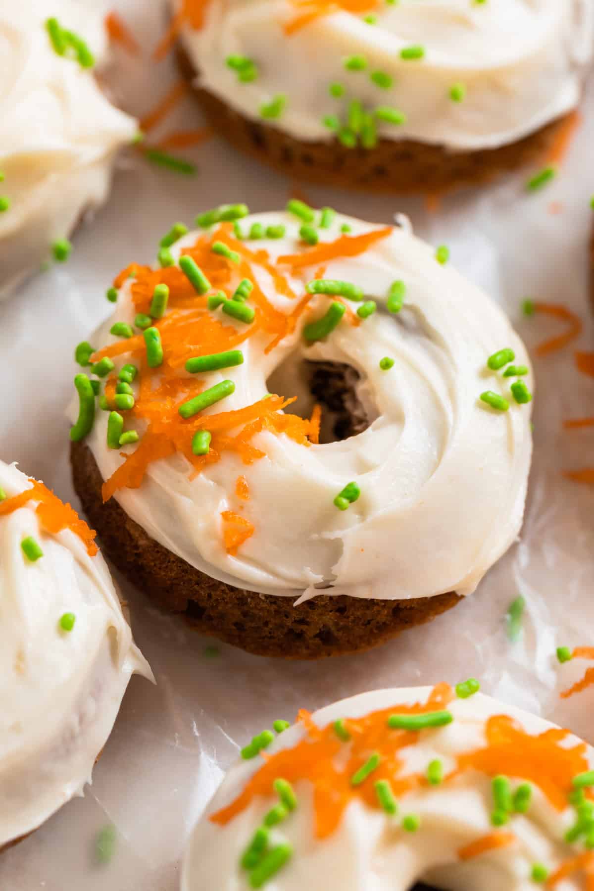 Carrot cake baked donuts with cream cheese frosting topped with shredded carrots and green sprinkles.