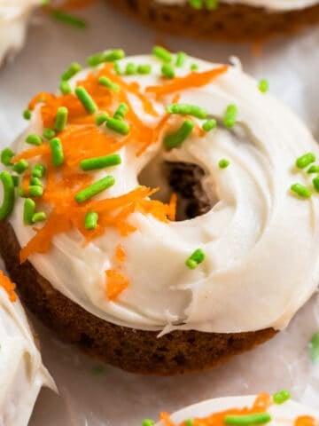 Carrot cake donut with cream cheese icing topped with sprinkles and shredded carrots.