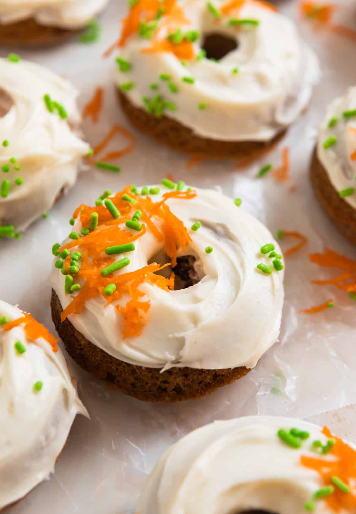 Carrot cake baked donuts with cream cheese frosting lined on parchment paper.