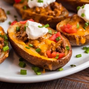 Cheeseburger stuffed potato skins on white dish with sour cream and chives on top.