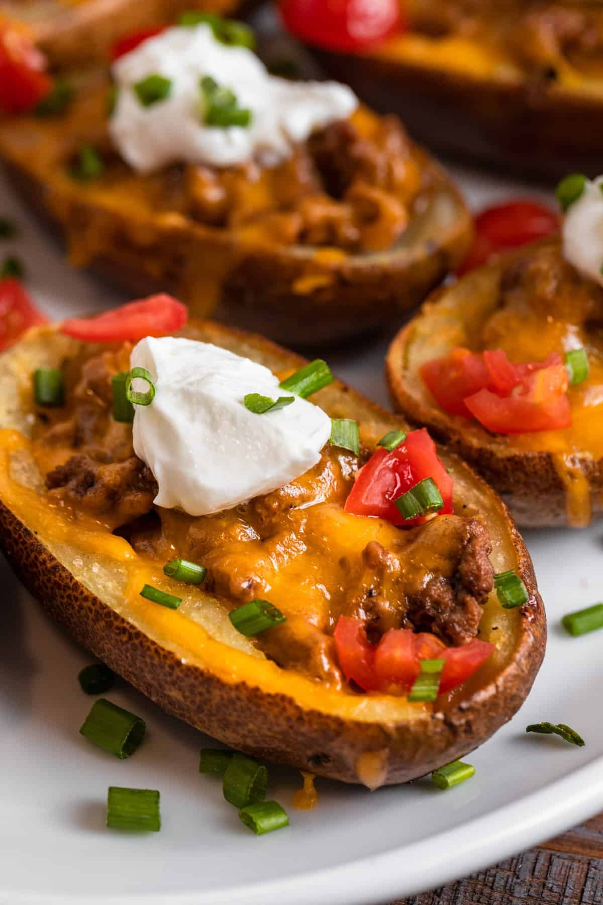 Cheeseburger stuffed potato skins on white plate topped with sour cream, chives and tomatoes.