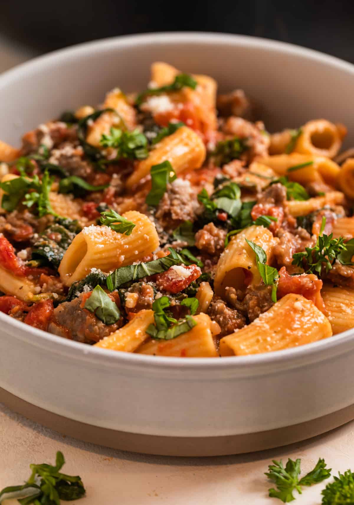 Bowl of spicy pasta Italian sausage pasta topped with chopped parsley and basil.