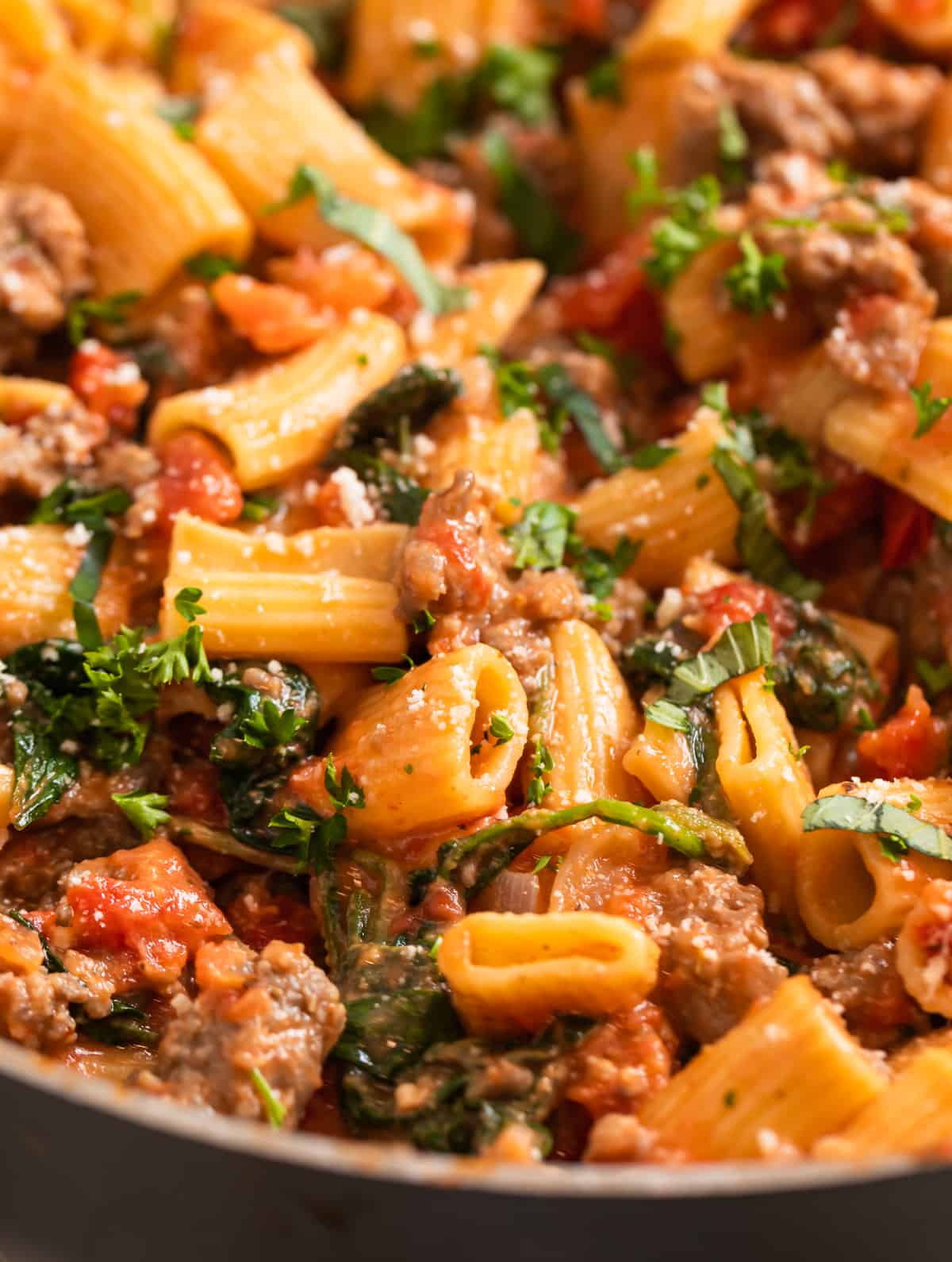 Spicy Italian sausage pasta in skillet with chopped basil and parsley.