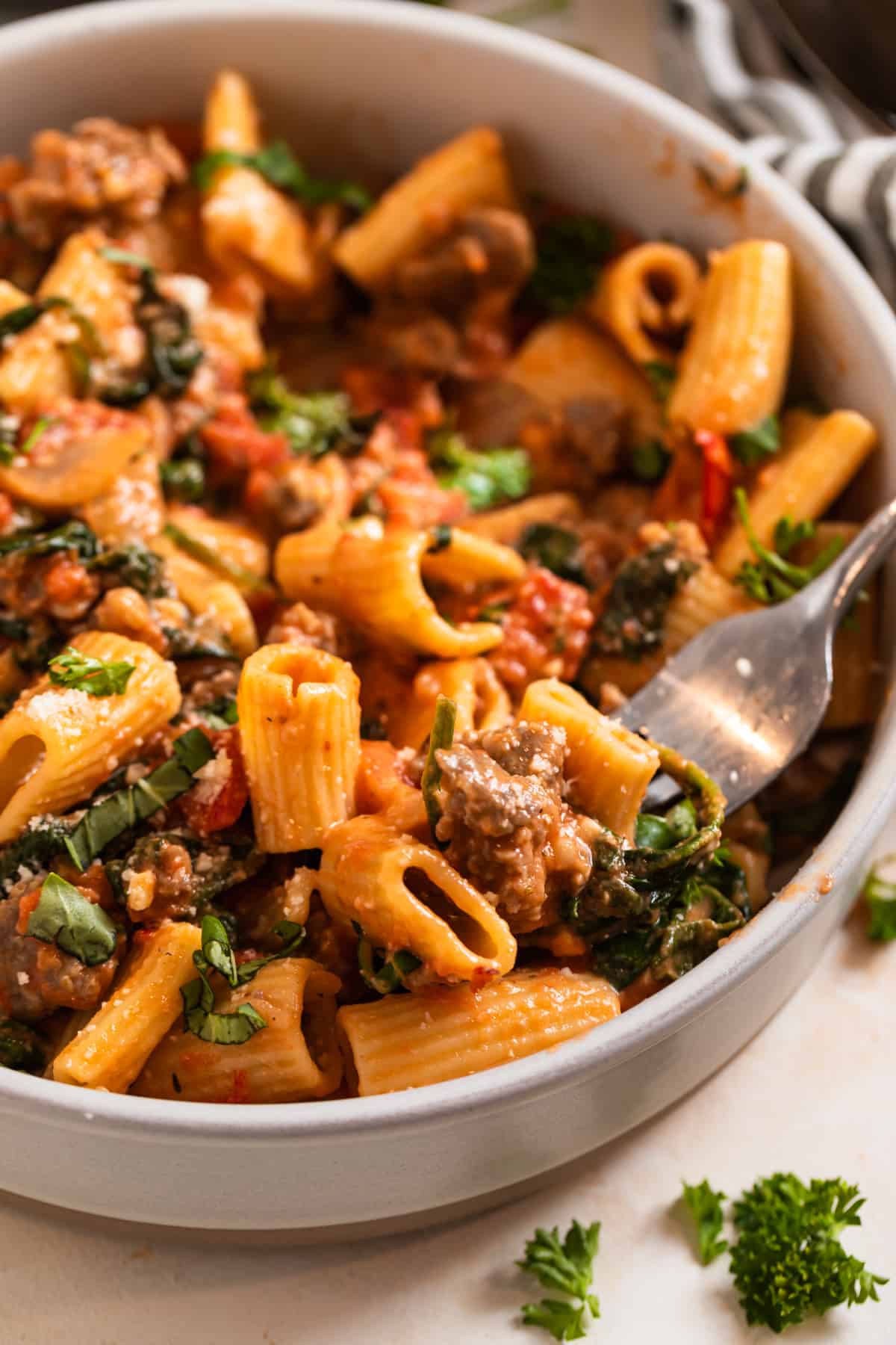 Bowl of pasta with Italian sausage, tomatoes and spinach with forkful of pasta.