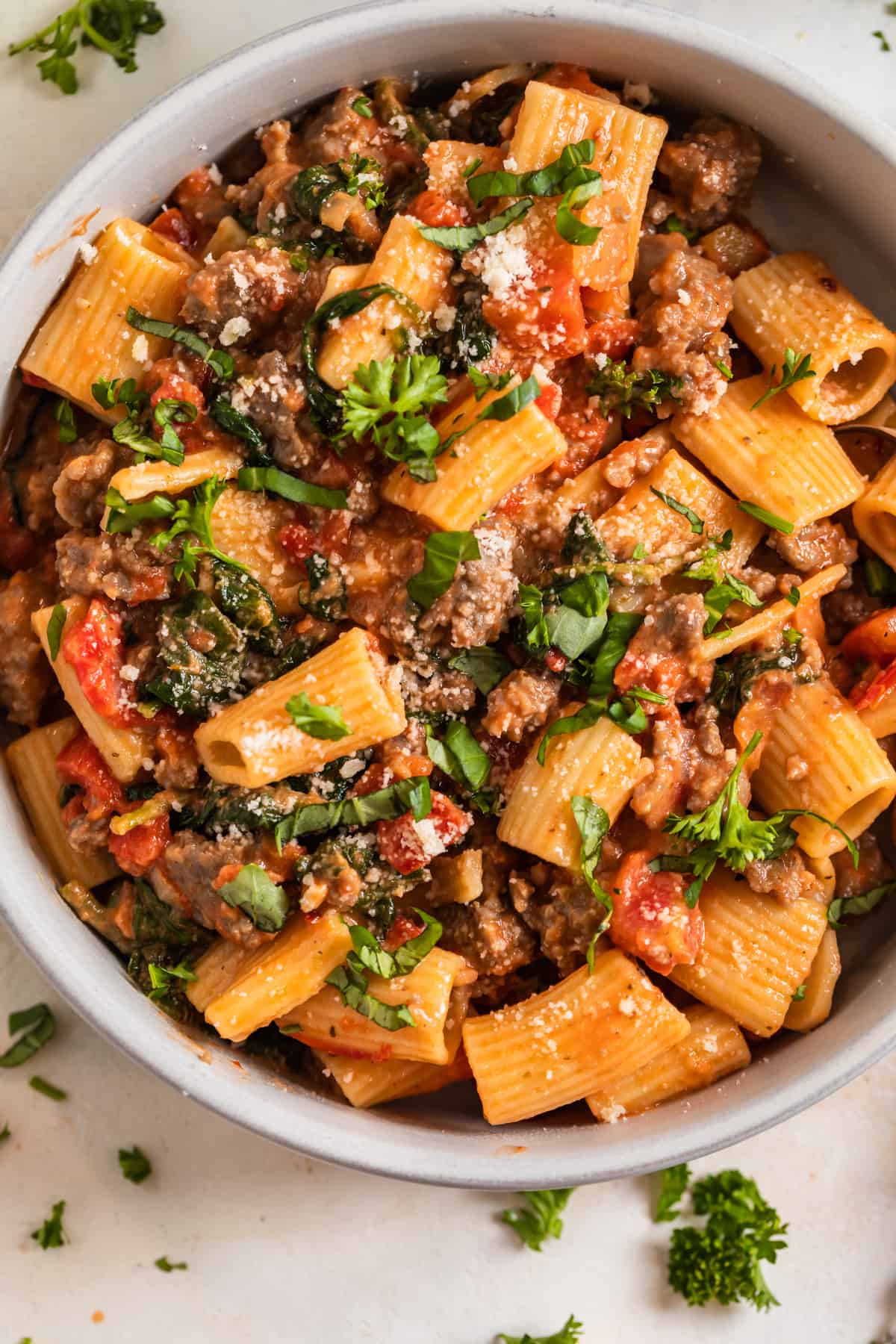 Bowl of spicy sausage pasta with chopped parsley and basil on top.