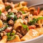 Bowl of Italian sausage spicy pasta with fork topped with parsley, basil and grated parmesan.