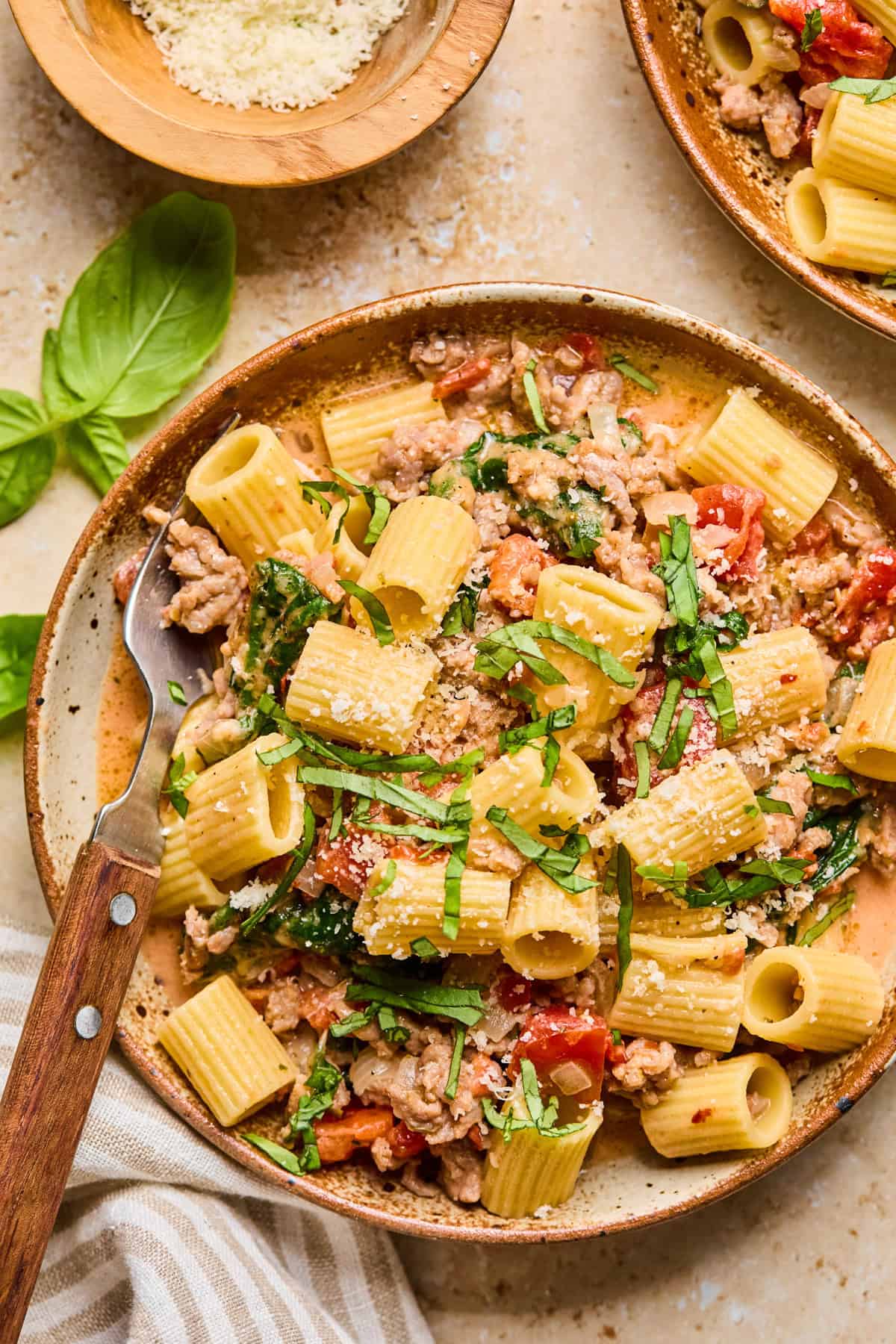 Dish with spicy Italian sausage pasta topped with parmesan and chopped basil.