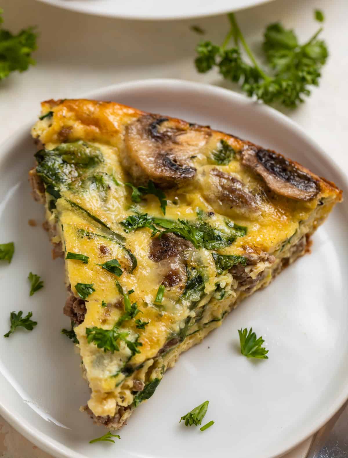Crustless mushroom quiche with beef, swiss and spinach on white plate.