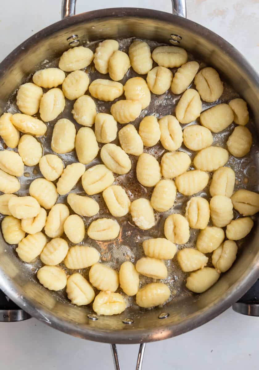 Uncooked gnocchi in silver skillet with butter.