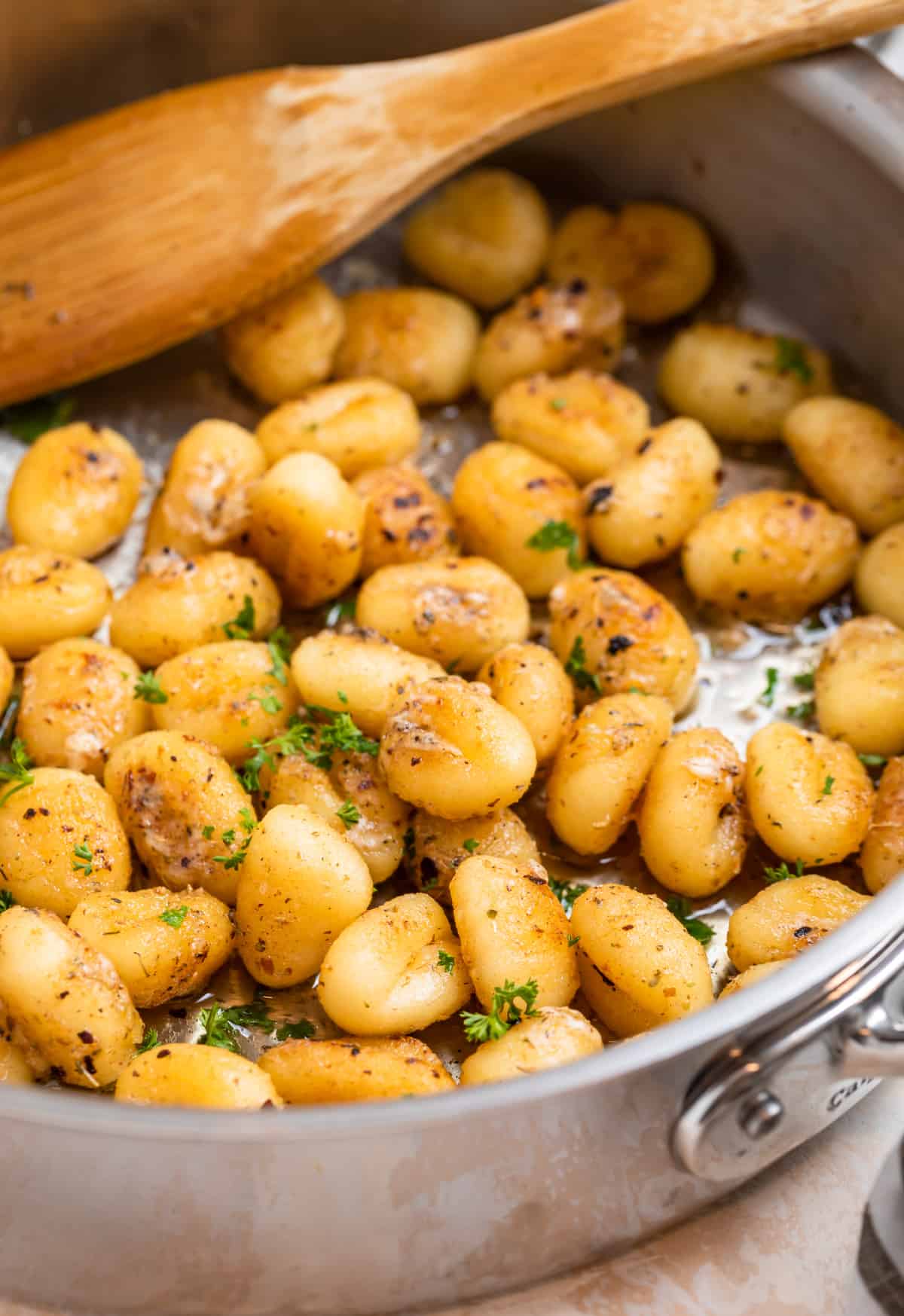 Pan fried gnocchi in skillet with chopped parsley and wooden spoon.
