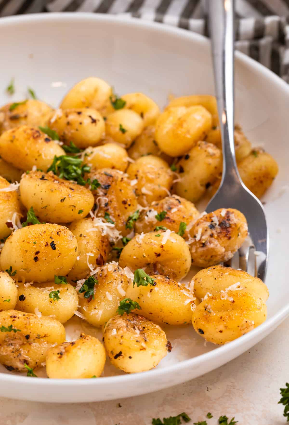 White plate with fried gnocchi topped with fresh parmesan and parsley.