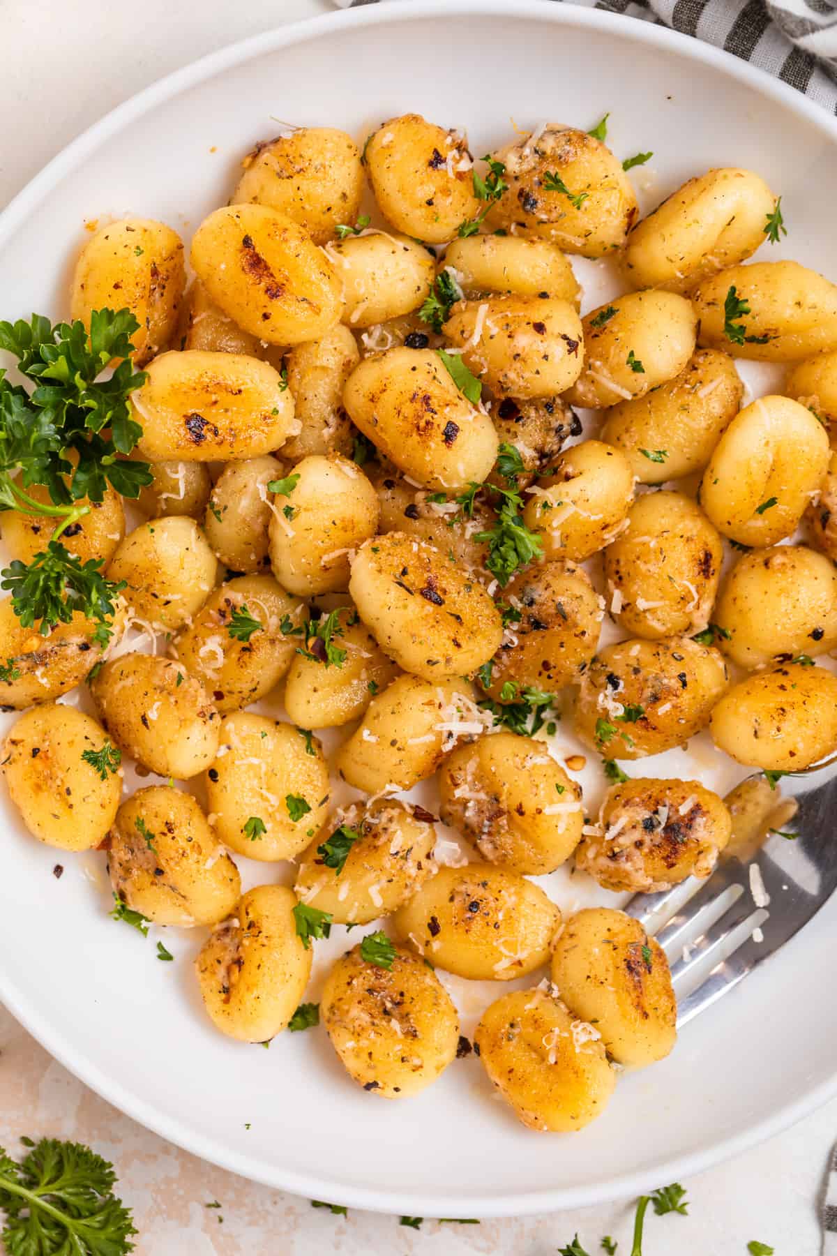 Overhead view of white plate with fried gnocchi topped with fresh parmesan and parsley.