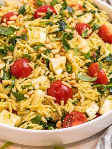Pesto orzo salad in white bowl topped with freshly chopped basil and toasted pine nuts.