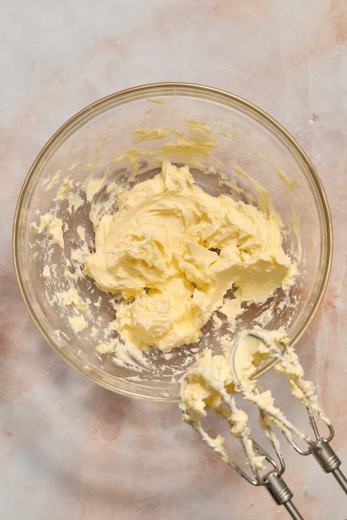 Creamed butter in glass bowl with electric hand mixer propped next to it.