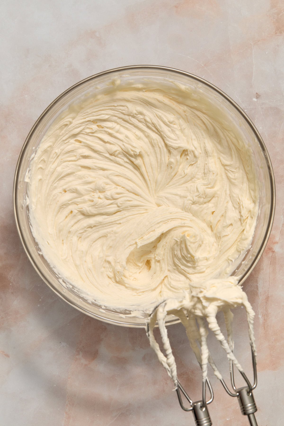 Prepped vanilla buttercream frosting in glass bowl with hand mixer.
