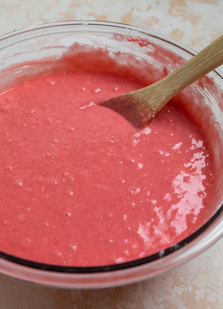 Strawberry cake mix batter in glass mixing bowl with wood spoon.