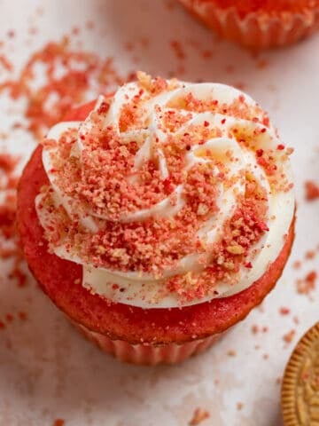 Strawberry cupcake with white icing and strawberry cookie crunch crumble on top.