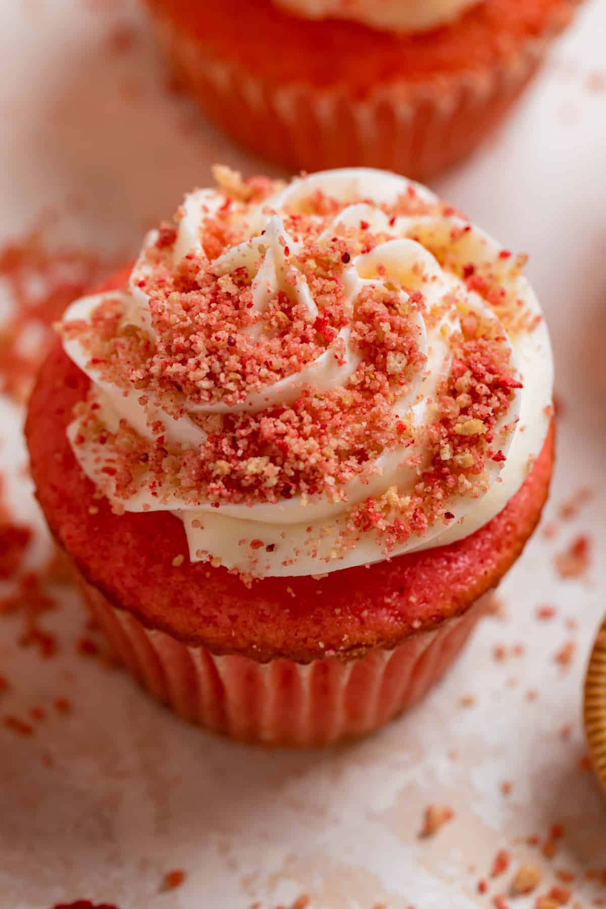 Strawberry crunch cupcakes with vanilla buttercream and strawberry crunch topping on counter with crumbs surrounding.