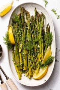 Lemon herb roasted asparagus on white plate with lemons.