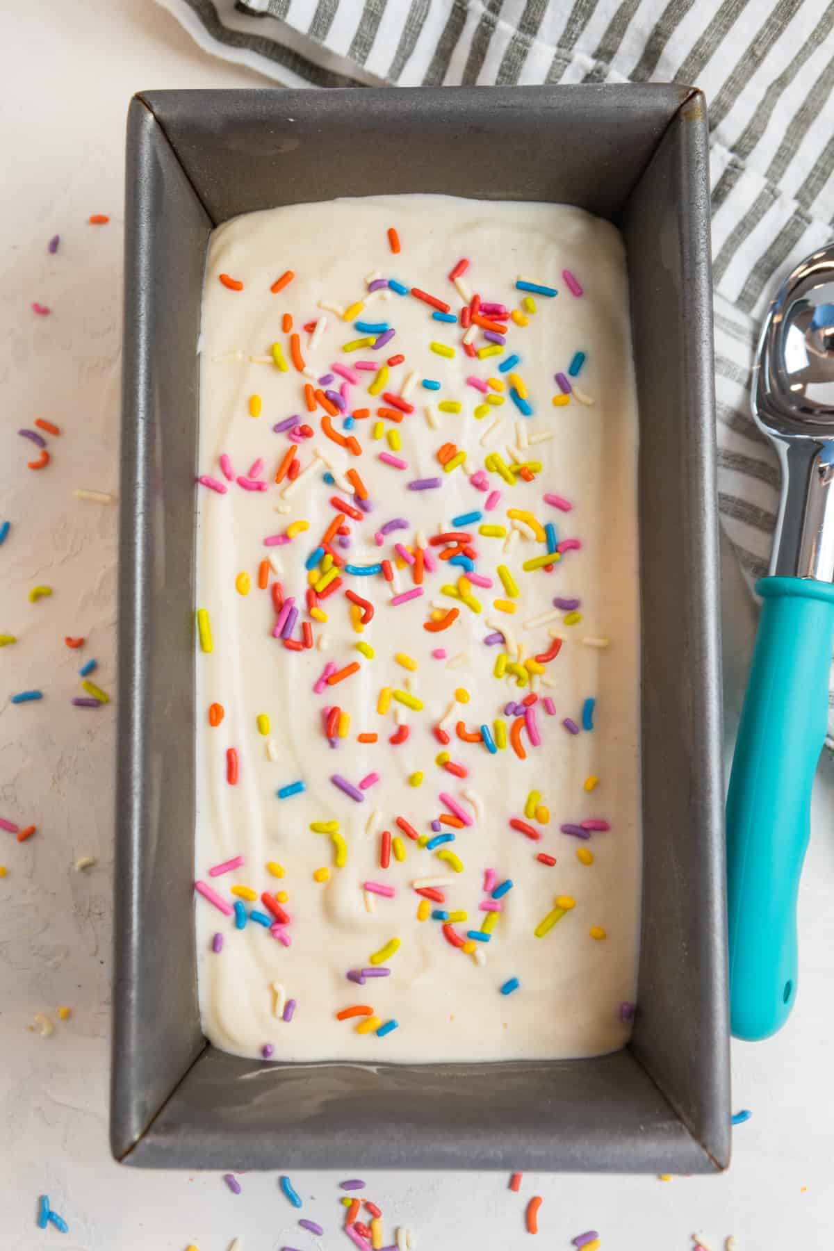 Protein cottage cheese ice cream in loaf pan with ice cream scoop and sprinkles on top.