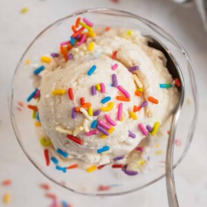 Scoop of cottage cheese ice cream in glass bowl with spoon and rainbow sprinkles on top.