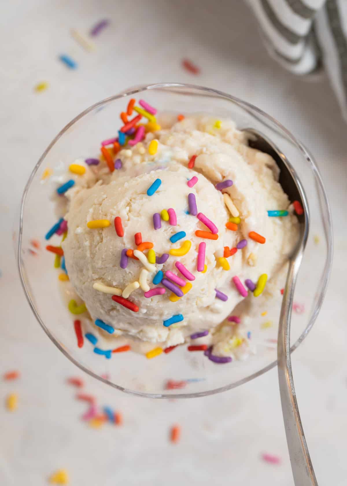 Cottage cheese ice cream scooped in glass dish with sprinkles on top and spoon scooping in.