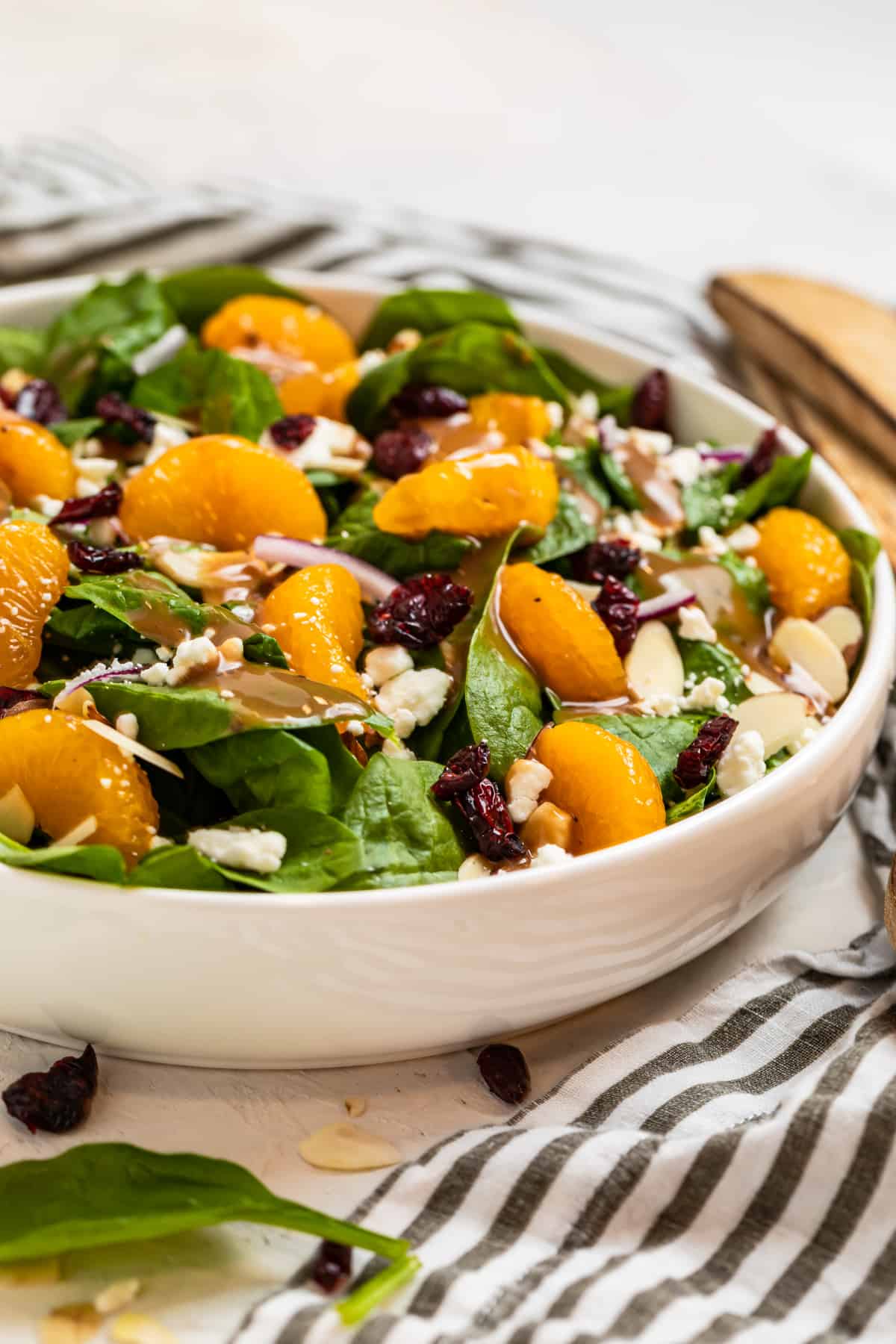 Spinach salad with mandarins, dried cranberries, toasted almonds, onion and goat cheese in white bowl.