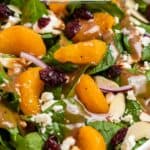 Spinach salad with mandarin oranges in white bowl topped with balsamic dressing.