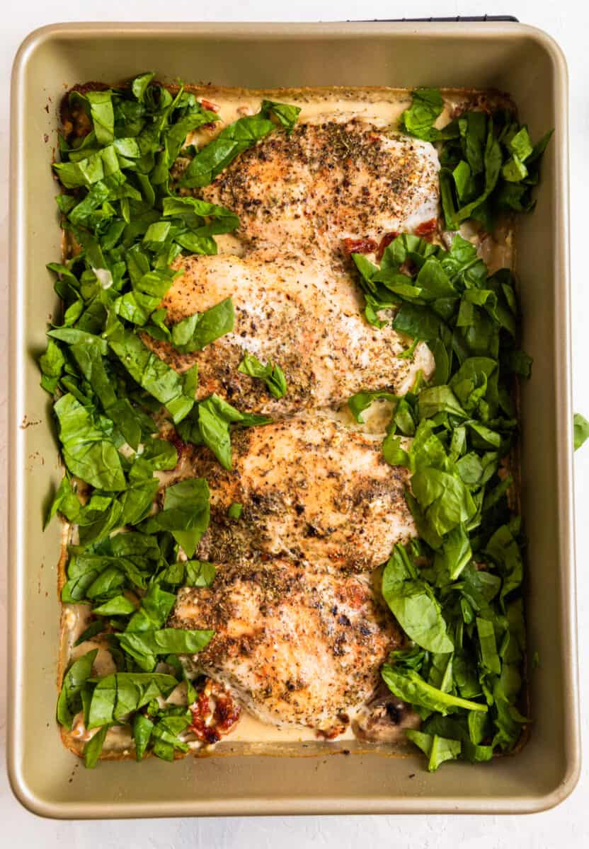 Spinach chopped and surrounding baked chicken breast in pan.
