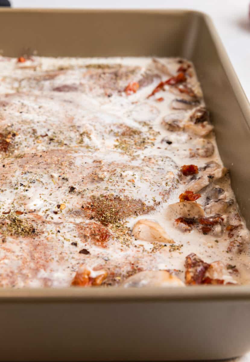 Baking pan with chicken breast, sun-dried tomatoes, mushrooms and creamy sauce over top.