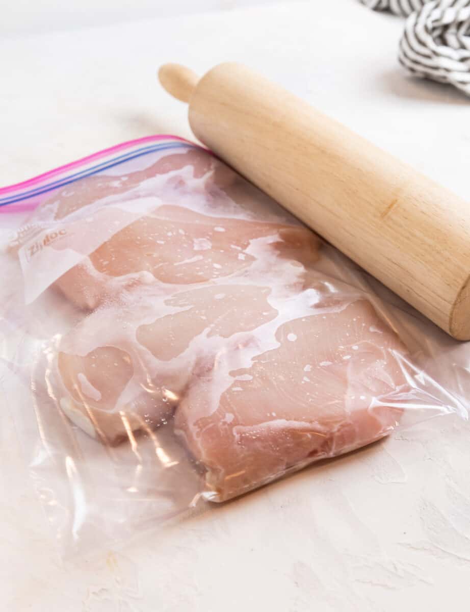 Chicken breast in plastic bag with rolling pin besied it.
