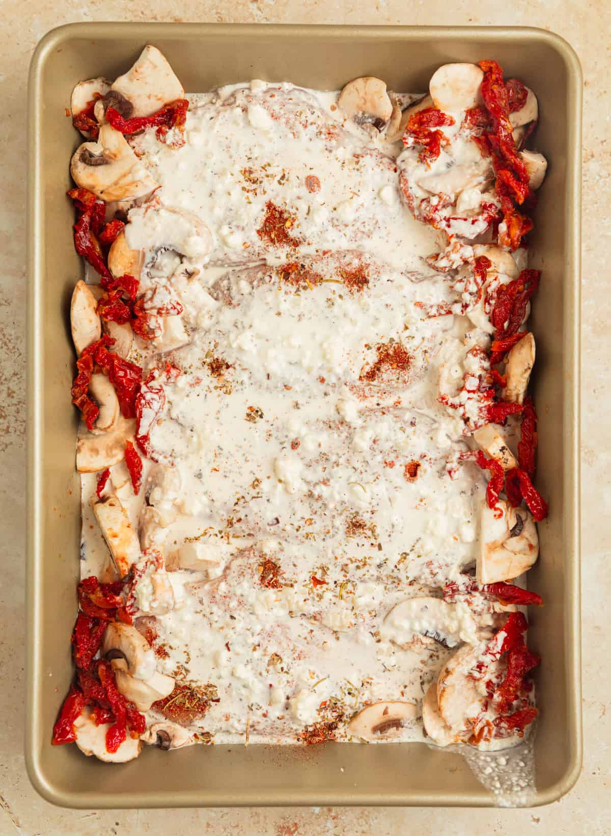 Cream sauce poured over seasoned chicken in pan before baking.
