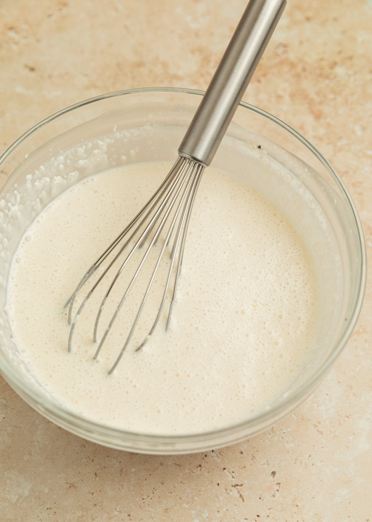 Cream sauce mixture in glass bowl with whisk propped in bowl.