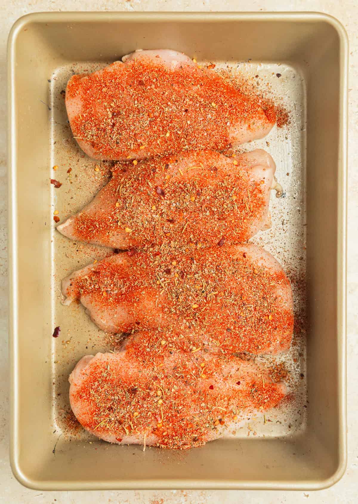 Seasoned chicken breasts lined in baking pan.