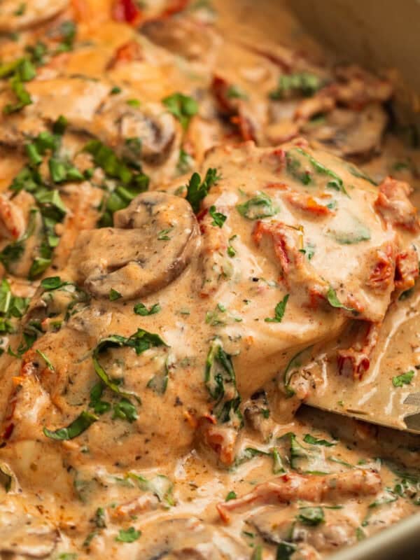 Serving spatula picking up piece of creamy baked tuscan chicken topped with mushrooms, parsley, etc.