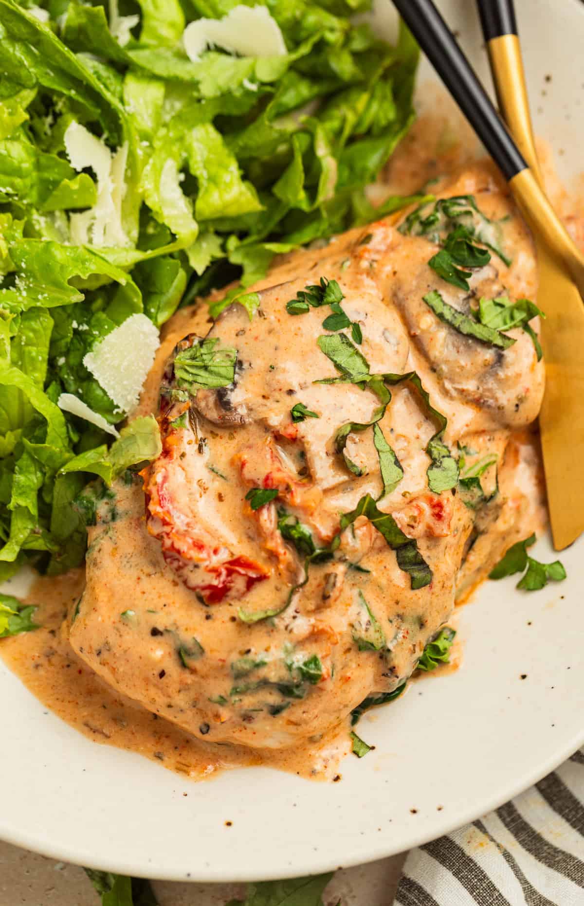 Creamy baked Tuscan chicken breast on white plate with salad and fork.