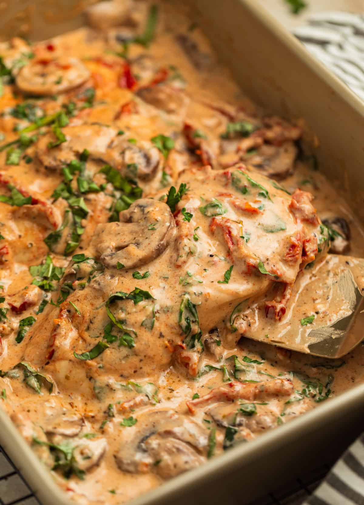 Pan with baked tuscan chicken and piece being picked up by spatula.