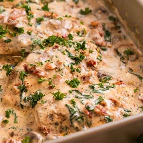 Creamy Tuscan chicken in pan topped with freshly chopped parsley, sun-dried tomatoes, spinach.
