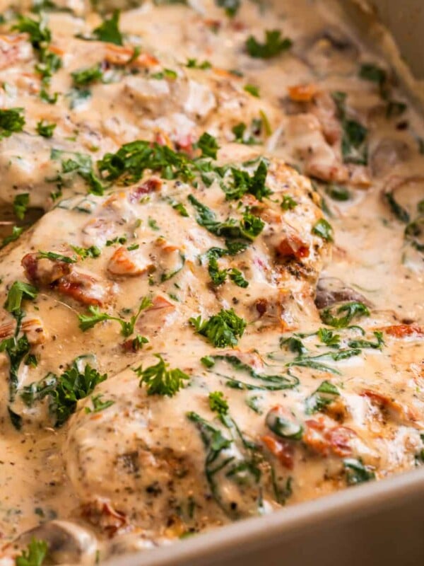 Creamy Tuscan chicken in pan topped with freshly chopped parsley, sun-dried tomatoes, spinach.