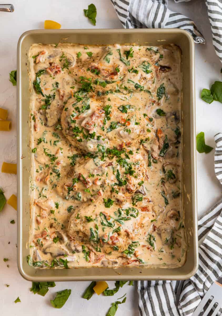 Baked Tuscan chicken in baking pan topped with chopped parsley.