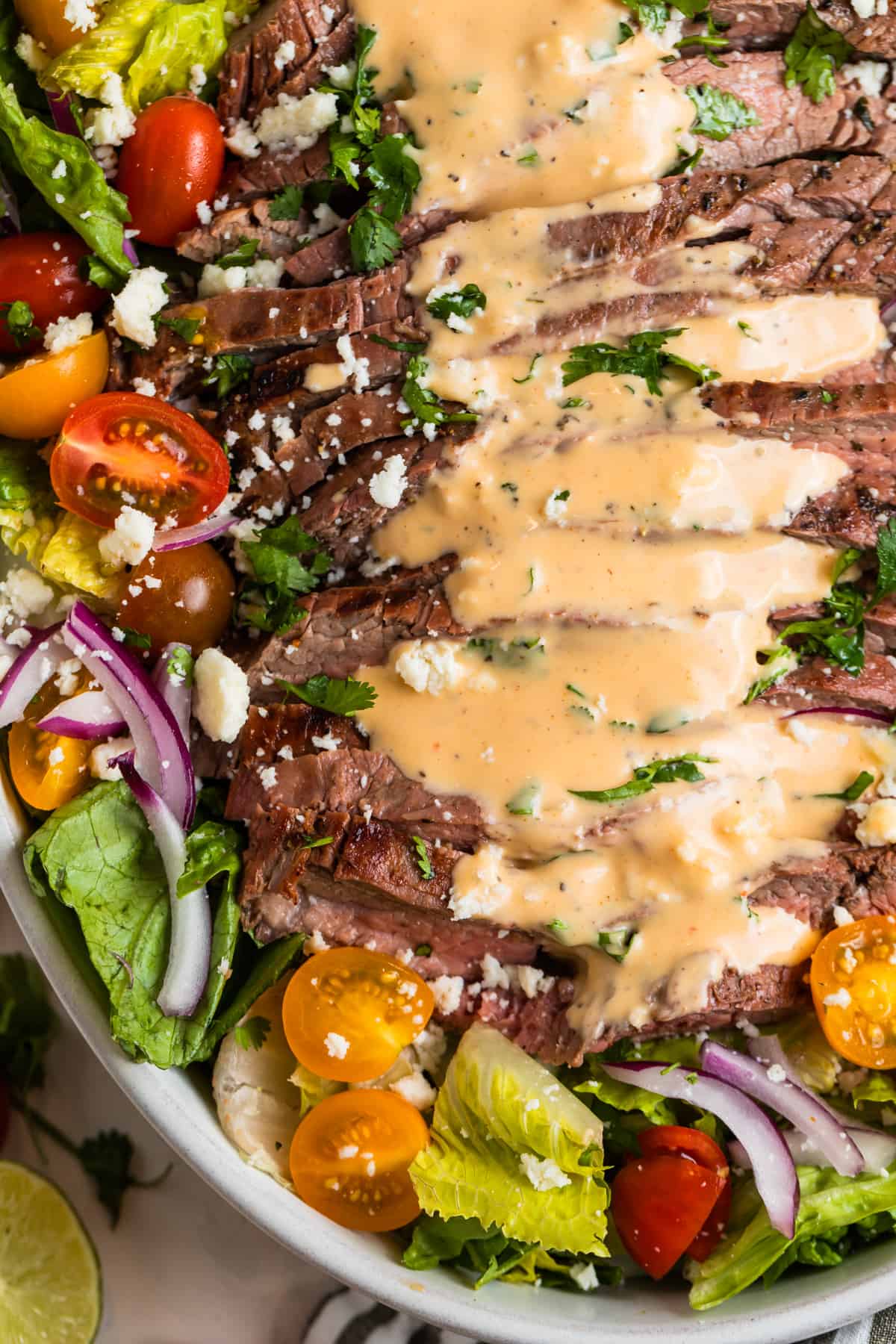 Grilled flank salad in dish topped with creamy sriracha dressing.