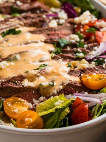 Grilled flank steak salad in dish topped with freshly chopped cilantro and cheese and sriracha dressing.