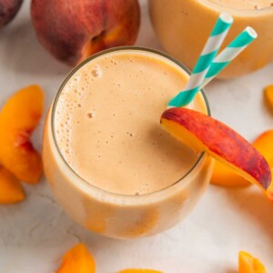 Peach banana smoothie in glass with peach slices surrounding.