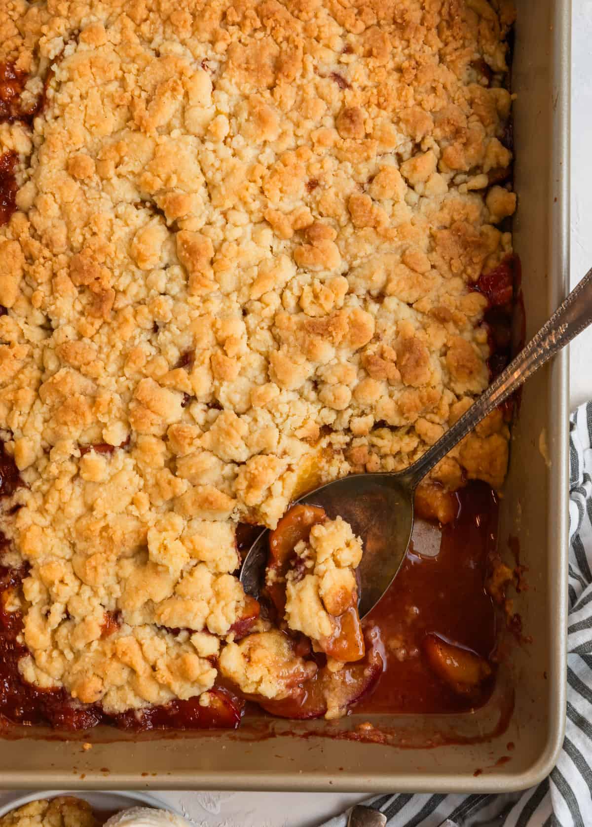 Cake mix peach cobbler in baking pan with spoon scooping out a section.