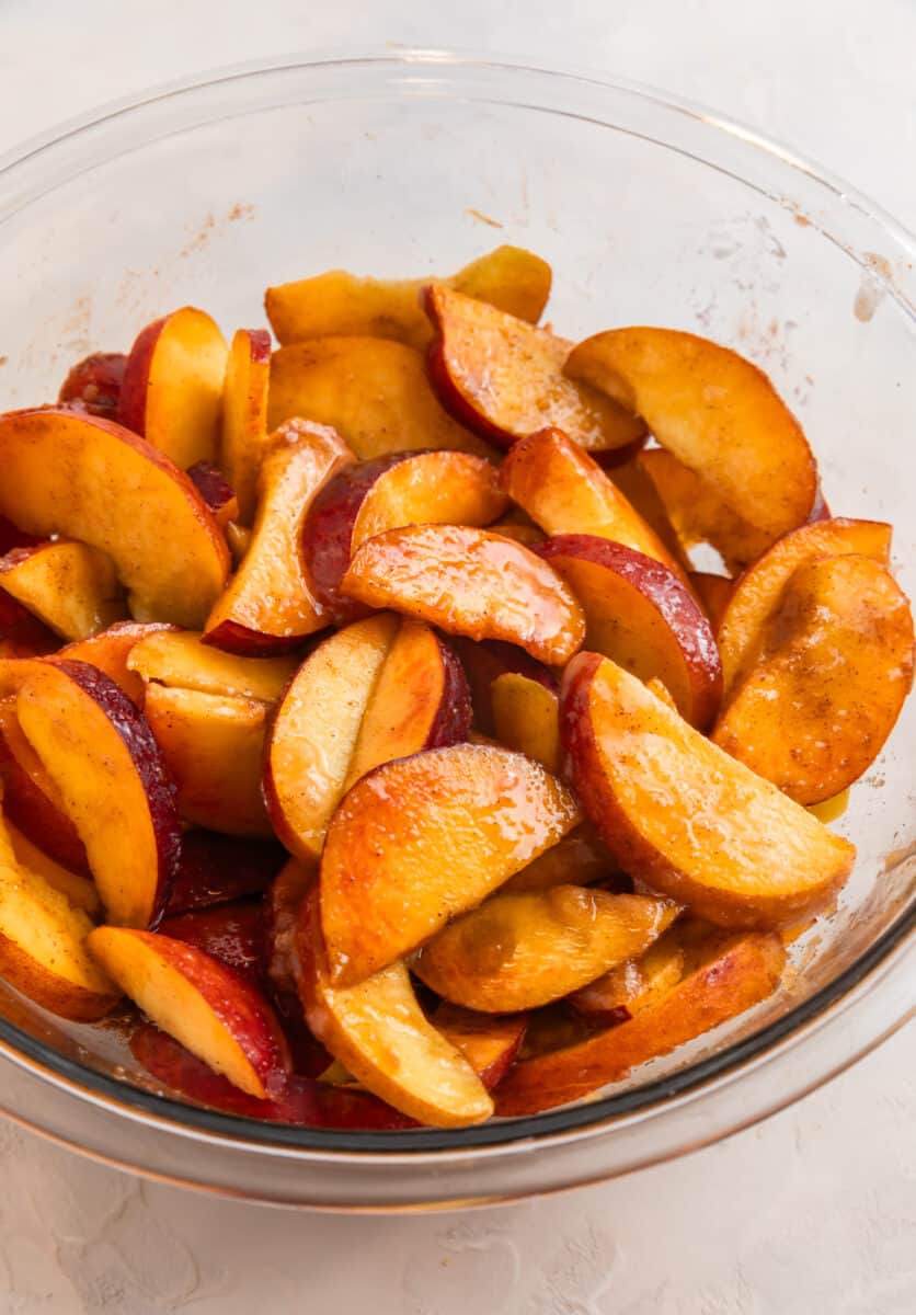 Peaches tossed with cinnamon, sugar and other ingredients in glass mixing bowl.