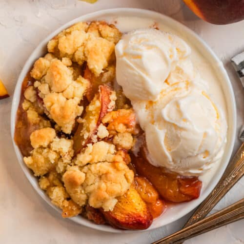 Overhead view of peach cobbler with cake mix on white plate with two scoops of vanilla ice cream.